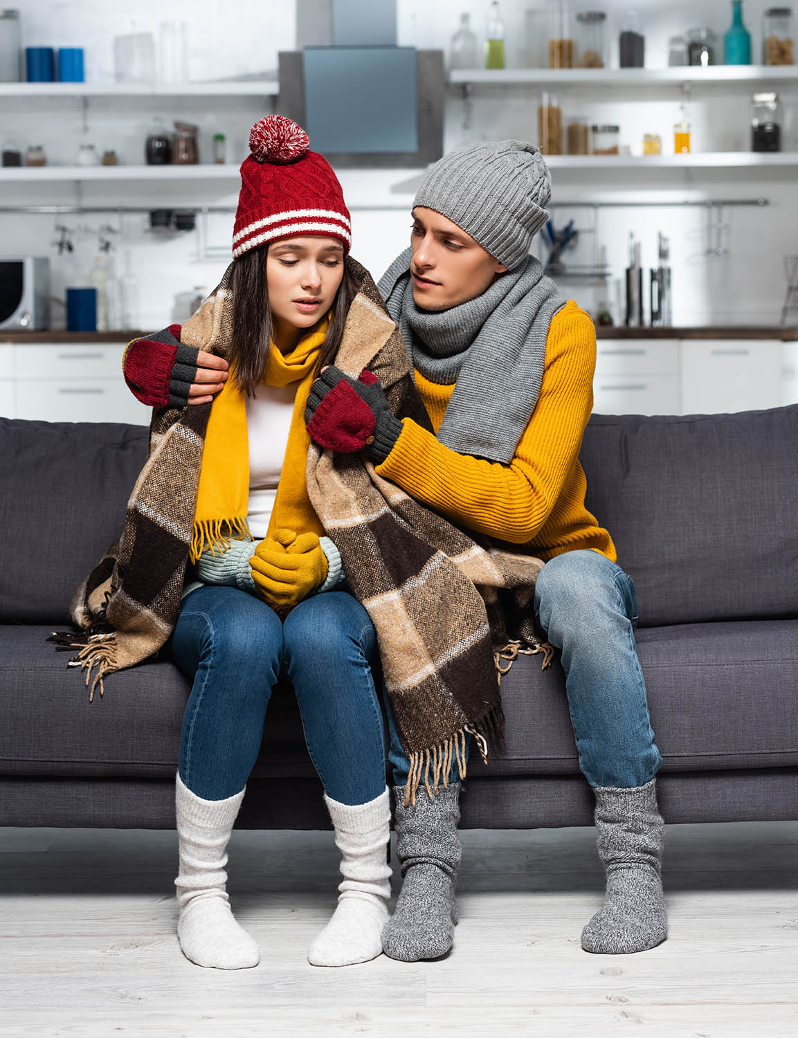 young man in warm hat and gloves covering freezing girlfriend wi