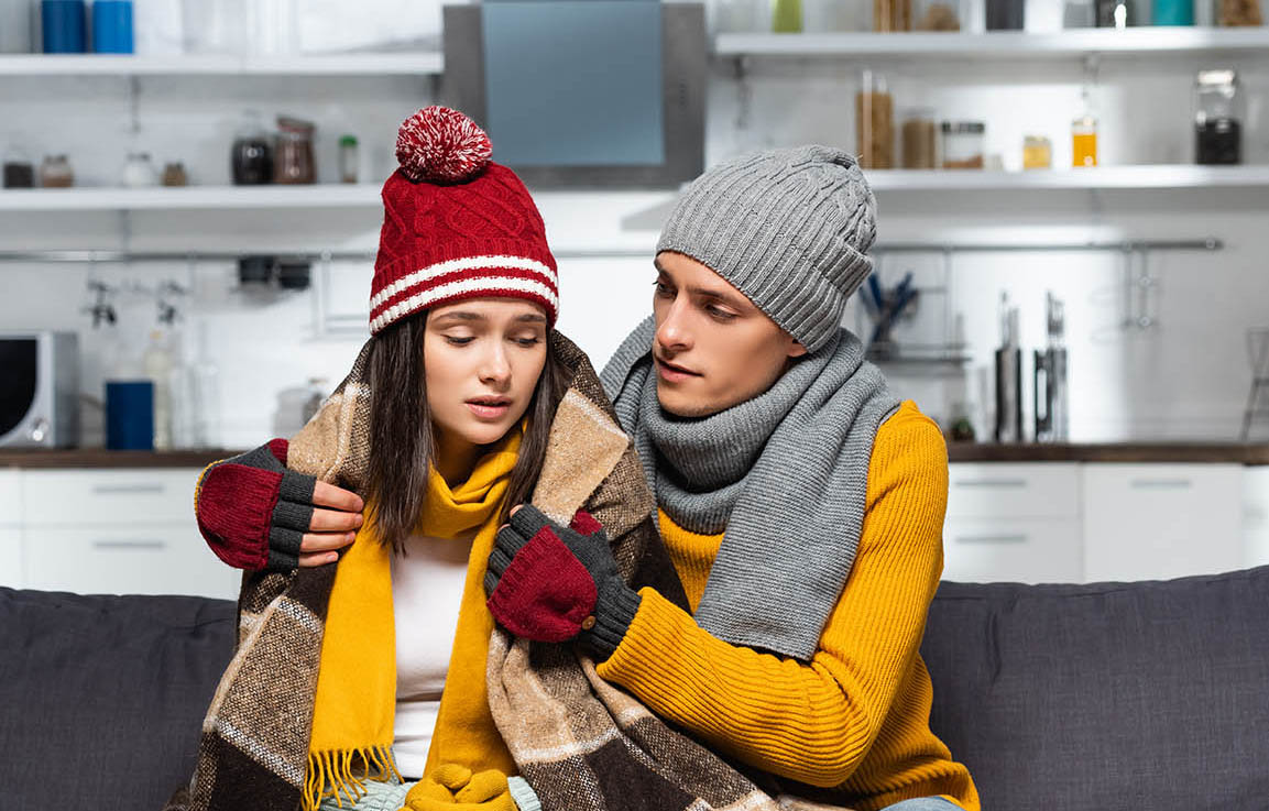young man in warm hat and gloves covering freezing girlfriend wi